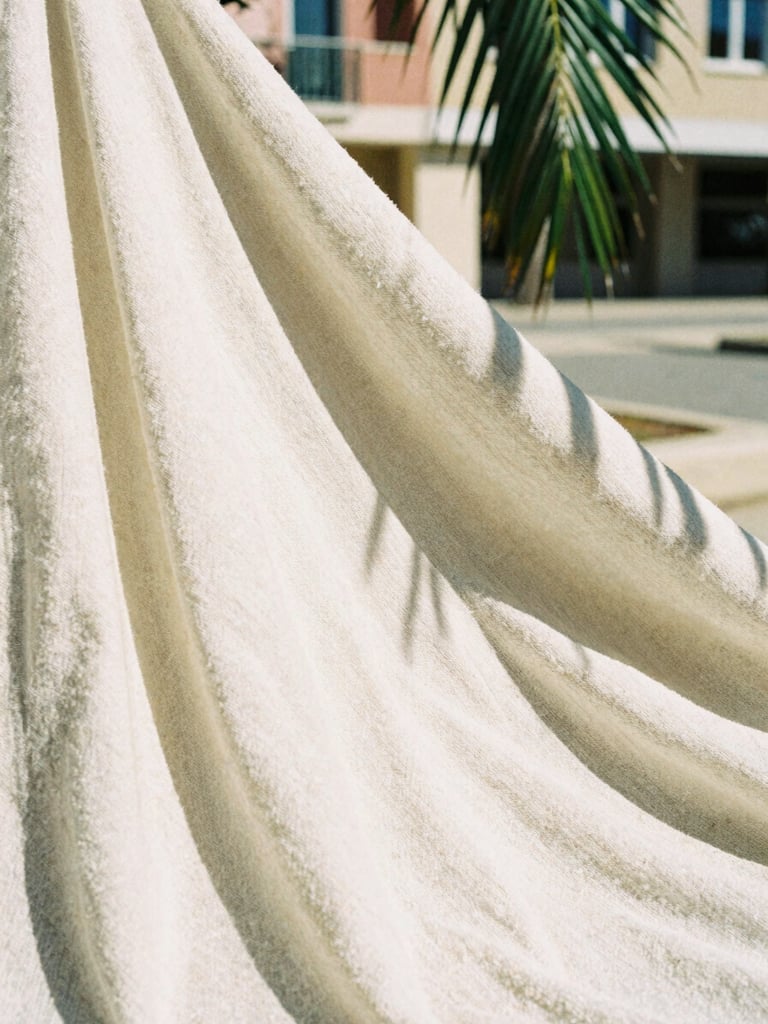 Close-up of thick organic cotton fabric texture, warm direct sunlight casting sharp shadows from a nearby palm leaf, architectural background, 35mm film.