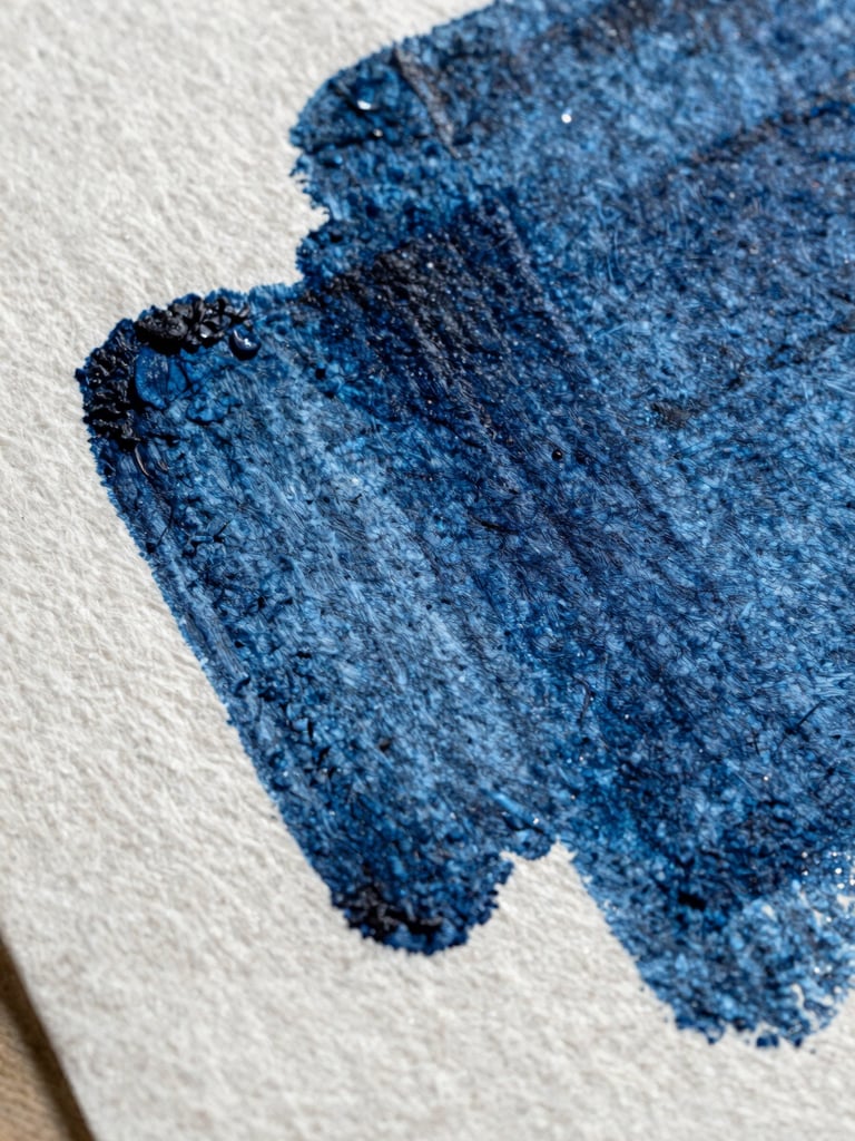 Extreme close-up of heavy-weight textured cotton paper with deep indigo ink pressed into the grain, casting a sharp shadow across the surface under harsh natural light.