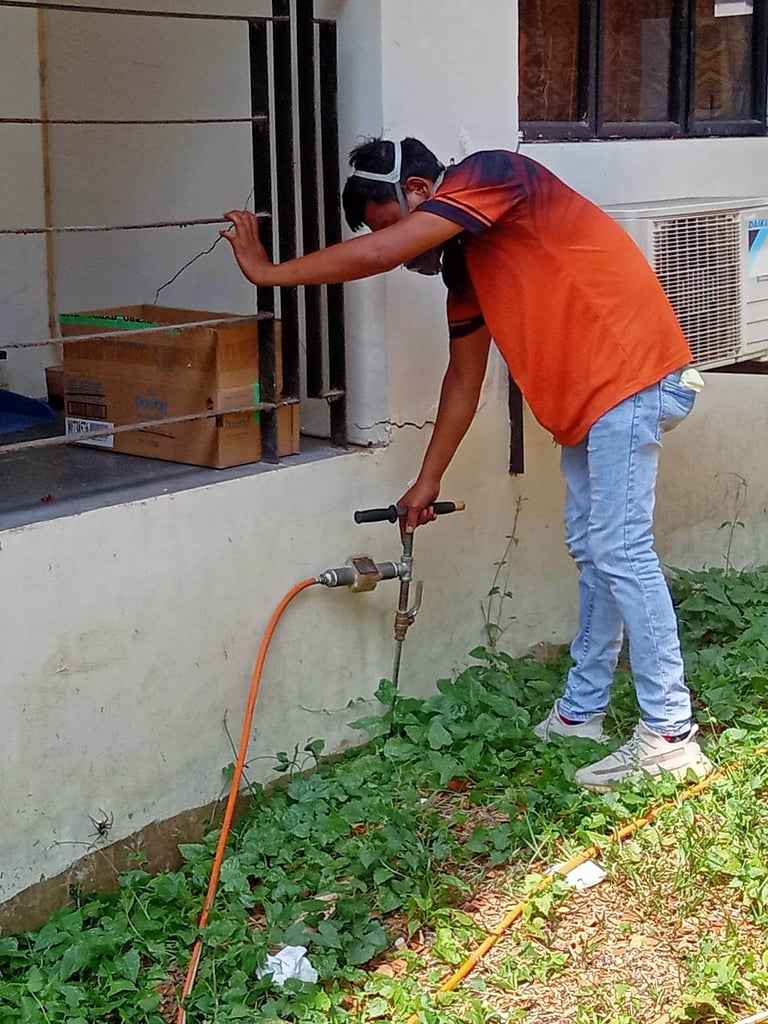 A pest control worker in an orange shirt performs professional soil injection treatment for termite prevention.