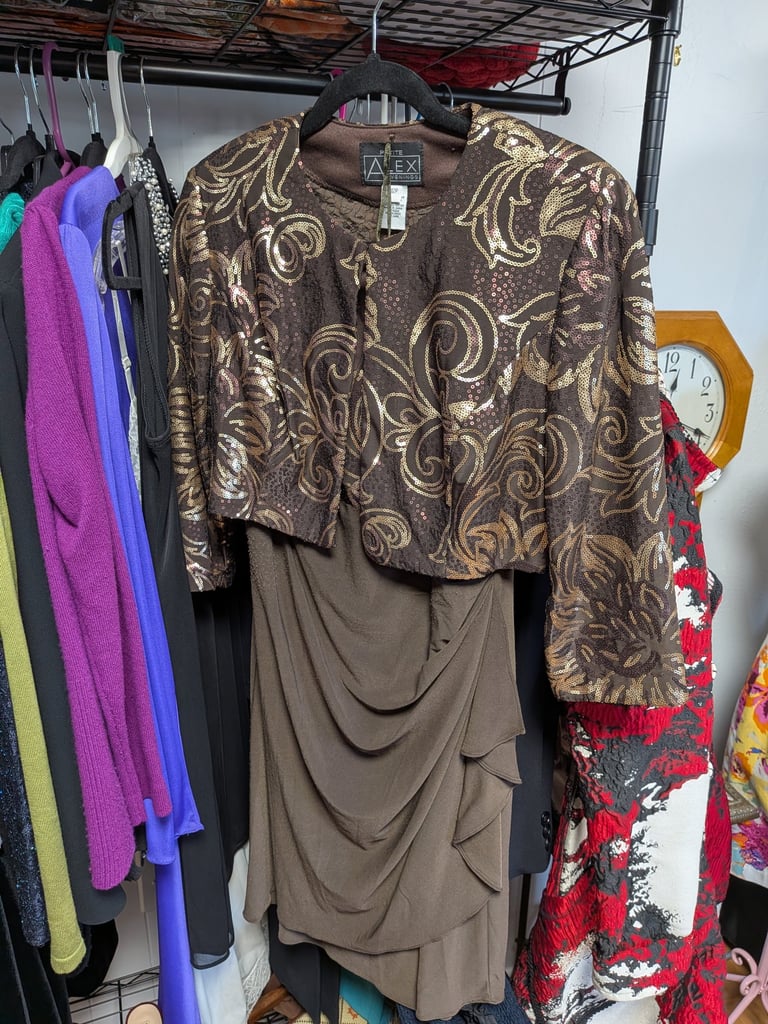 Elegant two-piece brown dress with a gold sequined floral bolero jacket hanging on a clothing rack.