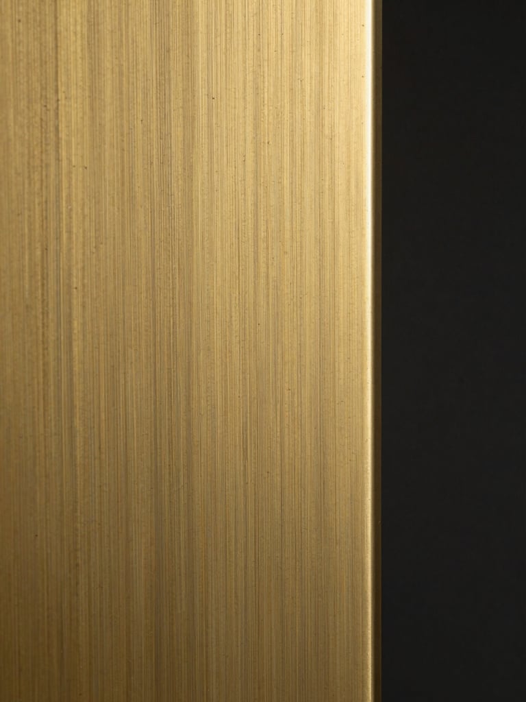 Extreme close-up of hand-finished brass panel surface under tungsten studio light, showing grain direction and subtle patina transition across the metal, tight crop isolating surface texture, dark background