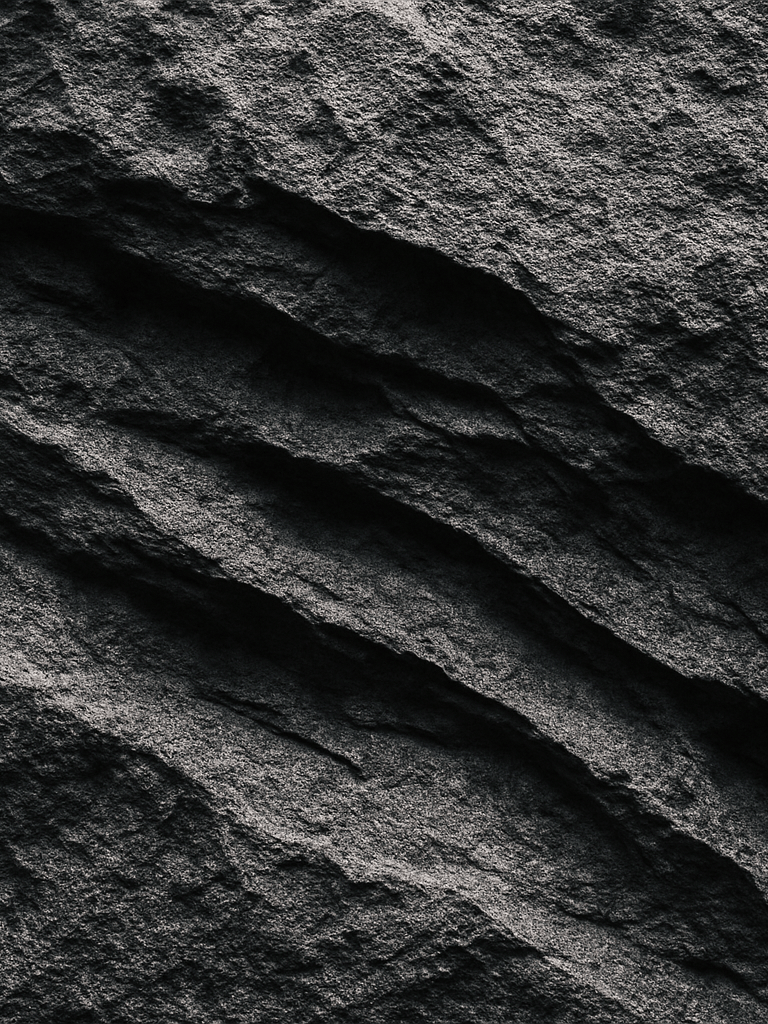 Extreme close-up of raw stone surface in cool gallery light, deep erosional marks and mineral grain visible, high contrast shadow geometry, no warmth, no styling, architectural framing