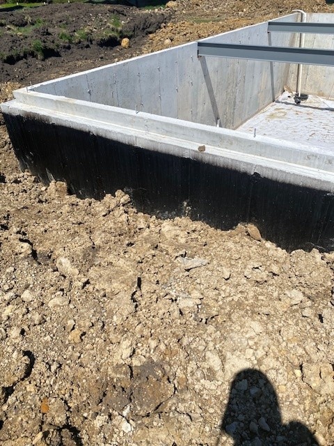 Concrete foundation walls with black waterproofing membrane at a residential construction site.