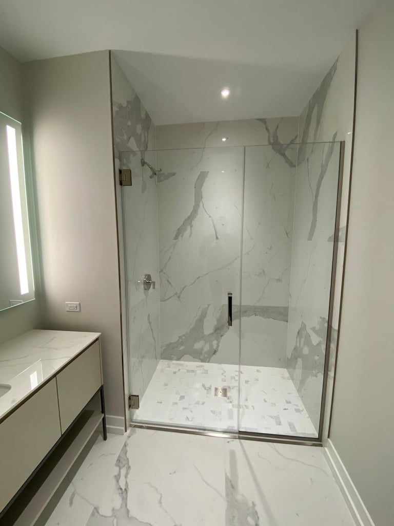 Modern master bathroom featuring a walk-in glass shower with marble walls and mosaic tile flooring.