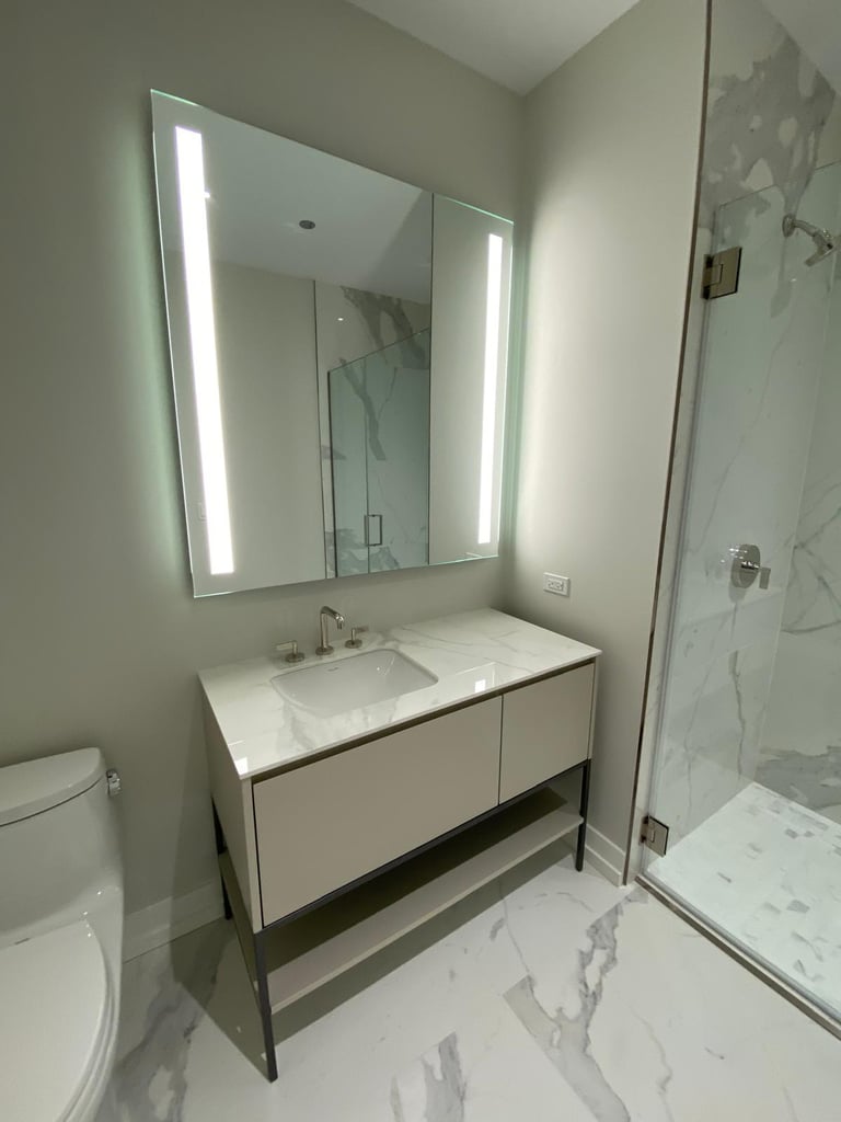 Modern bathroom featuring a light beige vanity, backlit LED mirror, and a marble tile walk-in shower.