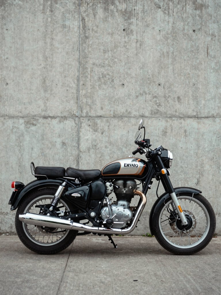 Wide three-quarter view of a Royal Enfield Classic 350 parked against a bare concrete wall in diffused north-facing daylight, frame geometry and chrome exhaust pipe fully visible, no rider present