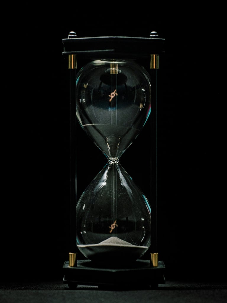 Elegant glass hourglass with white sand flowing against a dark black background.