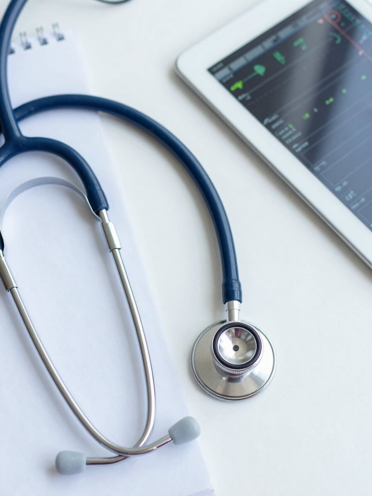 Overhead flat-lay of a modern stethoscope, clinical notepad, and a tablet displaying a patient chart with vitals, soft daylight, sterile white background.