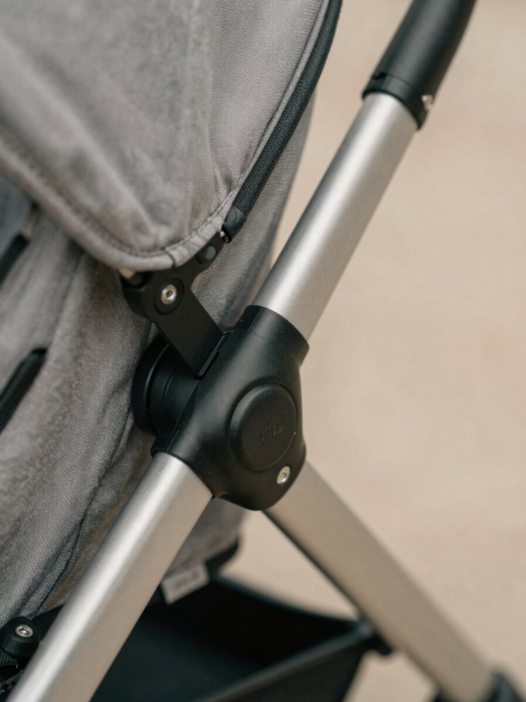 Macro detail shot of a stroller's reinforced mechanical folding joint, brushed steel and matte black finish, clean technical lines, soft daylight, 35mm
