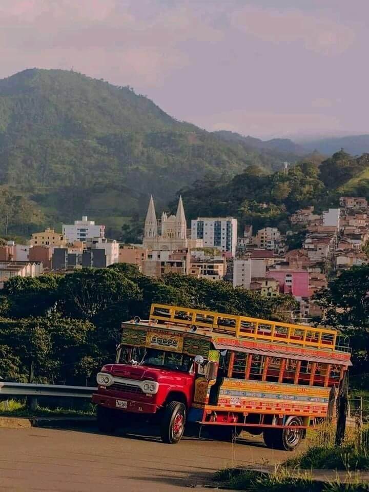 A colorful traditional Chiva bus parked on a mountain road with a scenic Colombian town view.