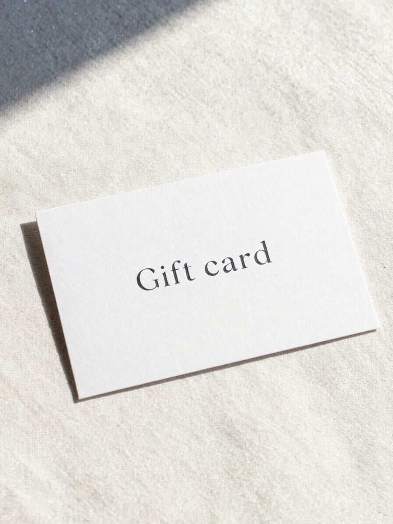 Minimalist high-end gift card on textured heavy paper, elegant typography, resting on a warm pearl-white linen surface, soft natural alpine daylight, glacier blue shadows, 35mm photography