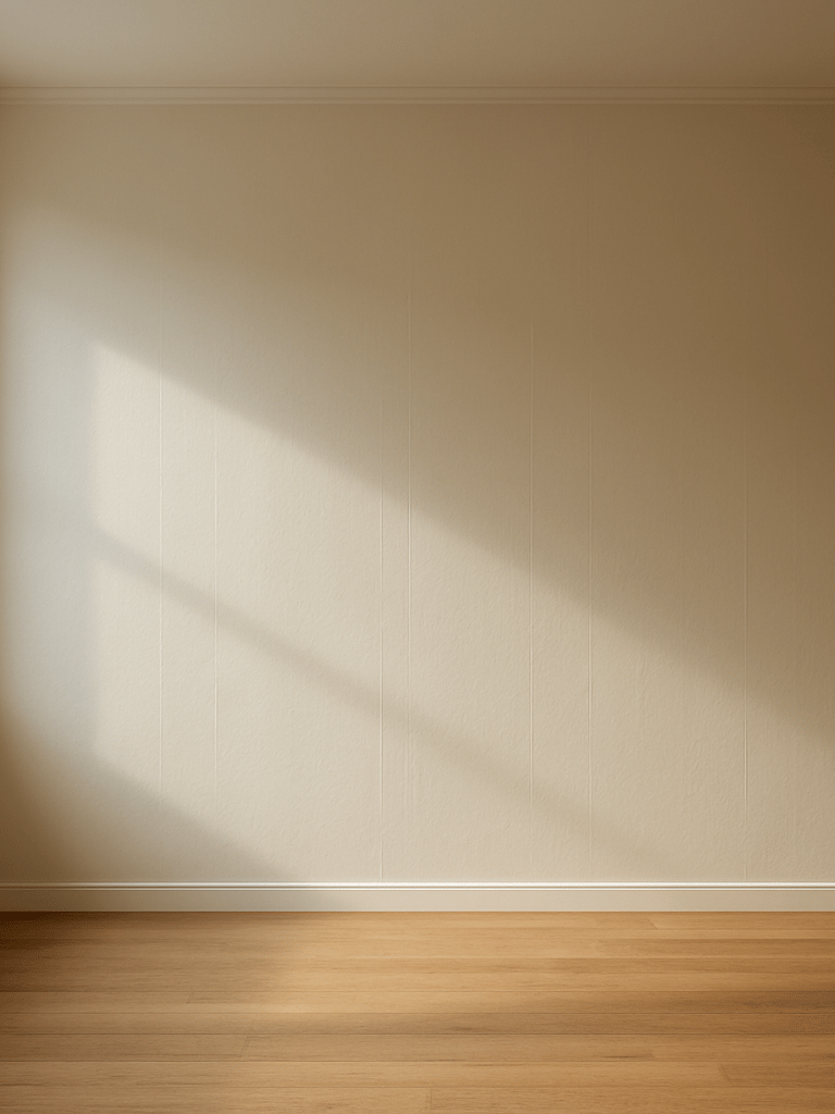 Wide room shot of a freshly painted living room wall in warm off-white, natural daylight streaming through a window to the left, clean roller lines visible on the smooth surface, no furniture, empty floor