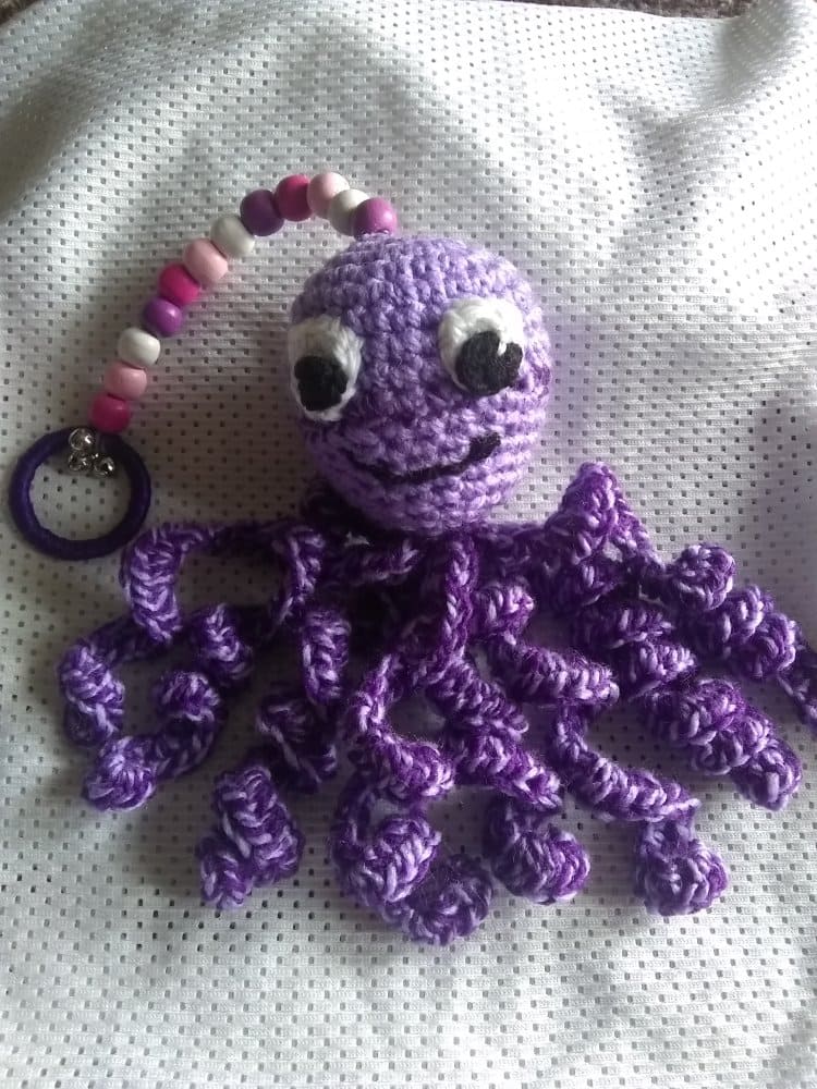 Pulpo de peluche morado hecho a mano a crochet con tentáculos rizados y un clip rosa con cuentas.