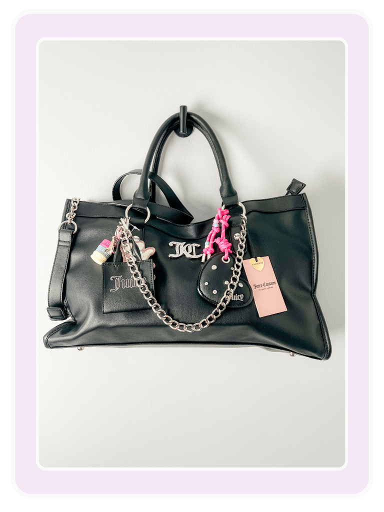 Black Juicy Couture tote bag with silver chain, logo hardware, and colorful charms hanging on a hook.