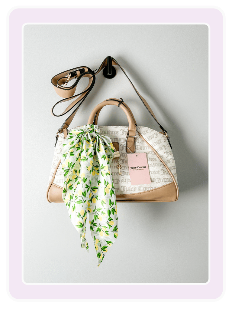 Cream Juicy Couture satchel handbag with tan trim and a lemon print scarf hanging on a wall hook.