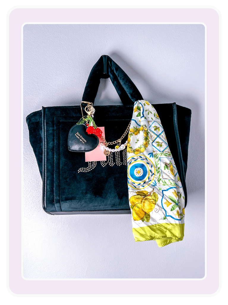 Black velvet Juicy Couture tote bag with heart charms and a lemon print silk scarf hanging on a wall.