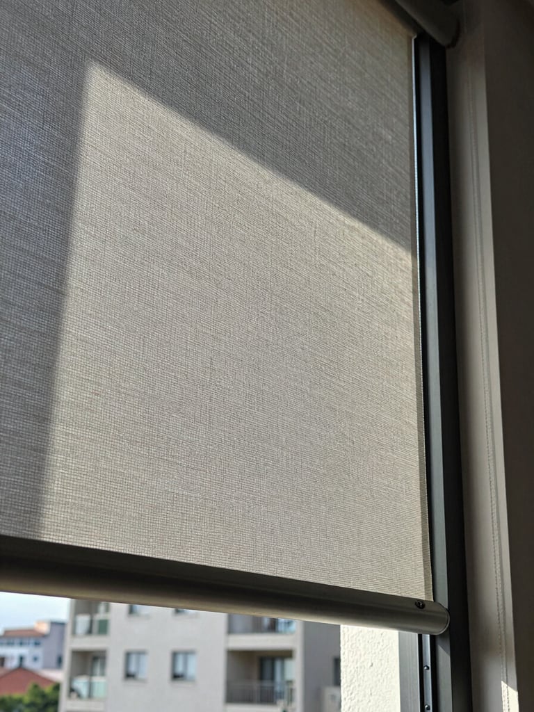 Extreme close-up of precision-cut roller blind fabric hanging against a tall residential window in Mexico City, cool north-facing daylight raking across the woven texture, aluminum bottom rail perfectly level, architectural plaster reveal visible at edge