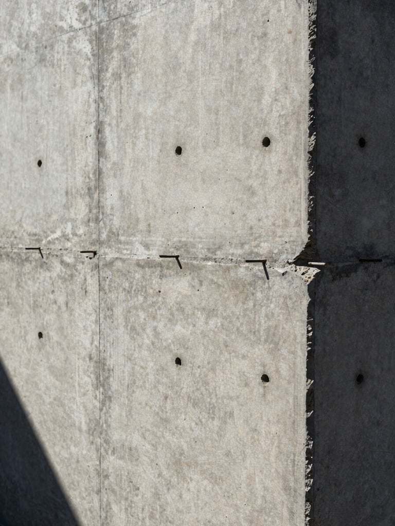 Extreme close-up of curing concrete wall with visible formwork tie holes, high-contrast shadows under harsh Baja sun.