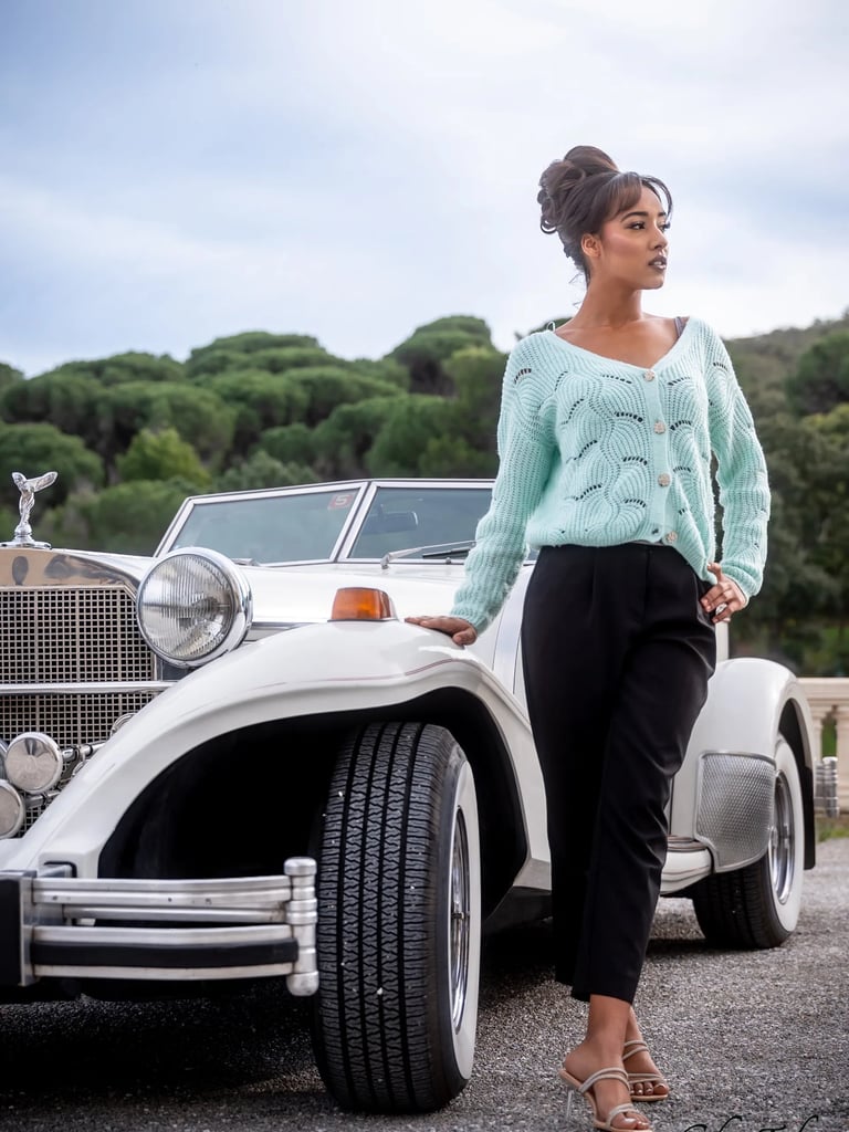 Femme en gilet mint posant devant une voiture de collection blanche en extérieur à Valmy 66.