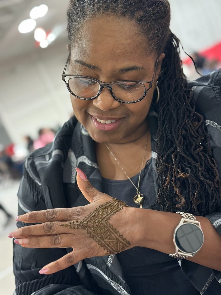 Black woman with glasses looks at the henna on her hand and smiles