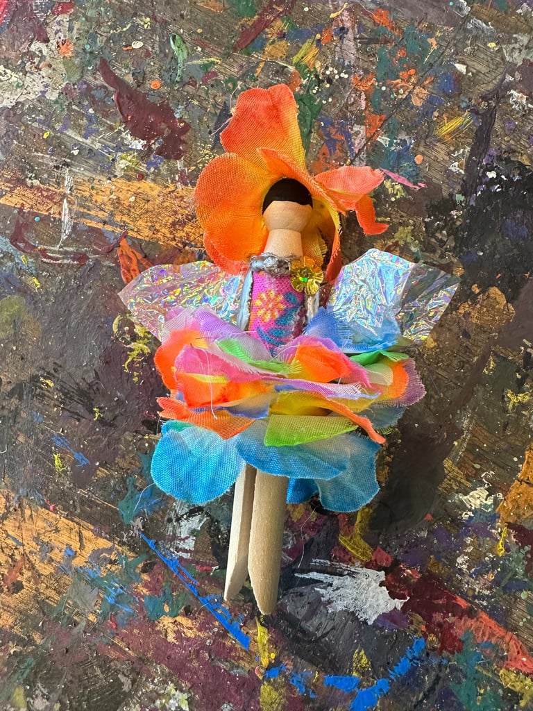flower fairy clothespin doll laying on a paint-splattered table