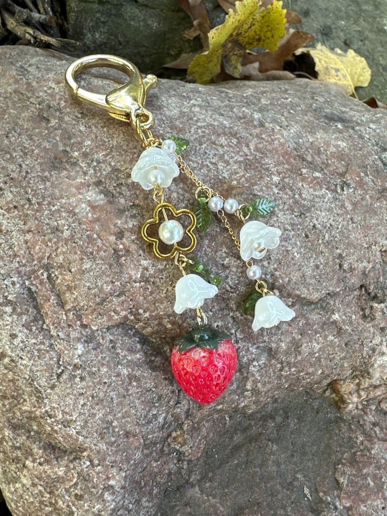 strawberry and flowers key chain with gold tone metal clasp and chain, laying on a rock