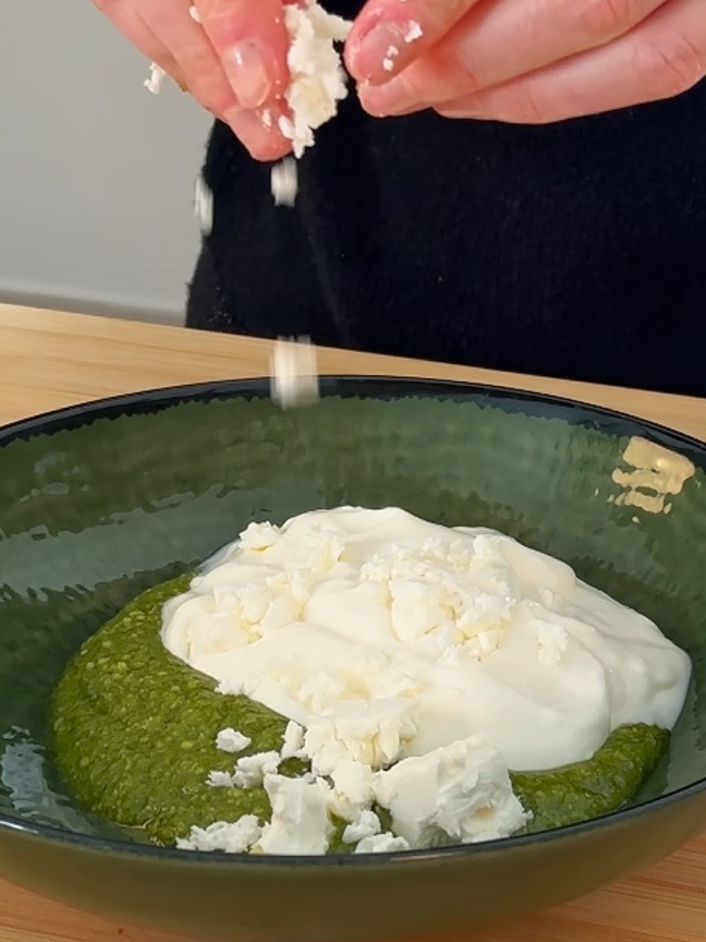 Unisci il pesto di basilico, la feta sbriciolata e la panna acida