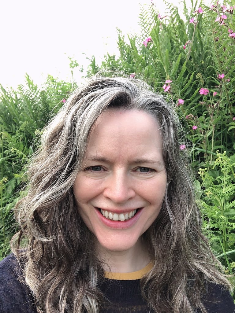 smiling woman with greying hair standing before wild flowers