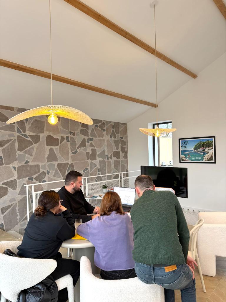 A team of young professionals collaborates at a table in a modern office with stone walls and pendant lighting.