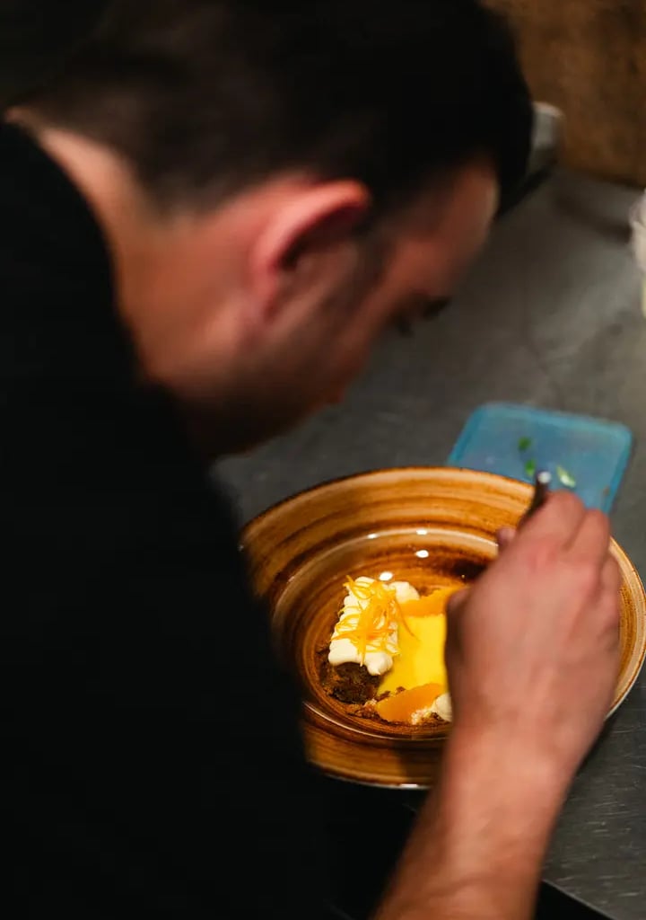 Nico, chef de Es Mestral, finalizando la presentación de un postre de naranja con crema y ralladura cítrica en la cocina del 