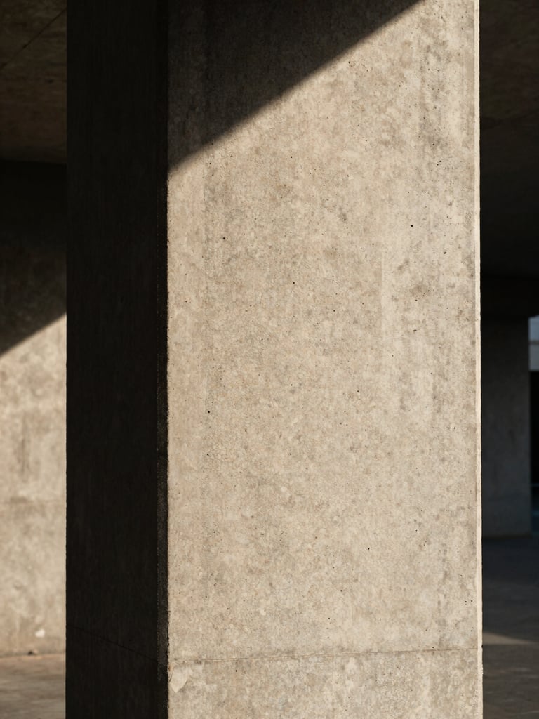 Vertical portrait of a concrete pillar under harsh afternoon sun, emphasizing the raw texture and sharp shadow line, eye-level perspective.