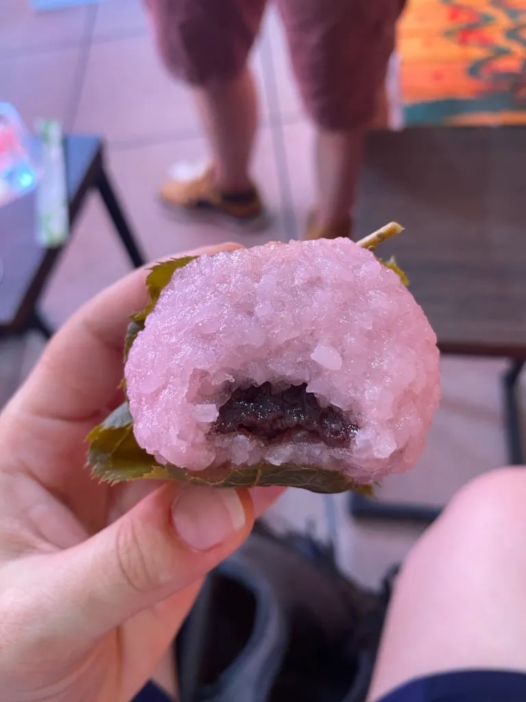 a person holding a pink sakura mochi with a anko inside
