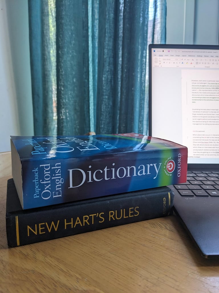 An Oxford English dictionary and New Hart's Rules style guide on a table next to a open laptop.