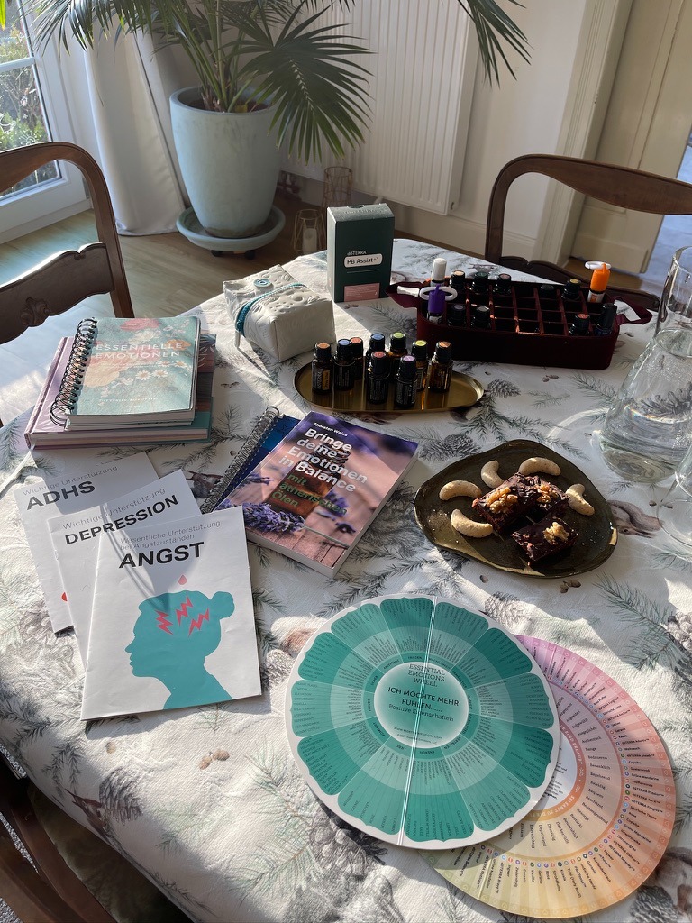 Essential oils, emotional wellness books, and an emotion wheel for mental health support on a table.
