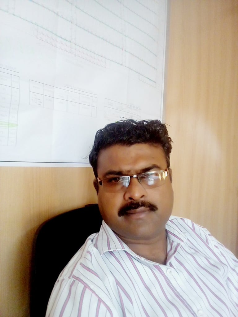 a man with glasses and a mustache sitting in front of a white board