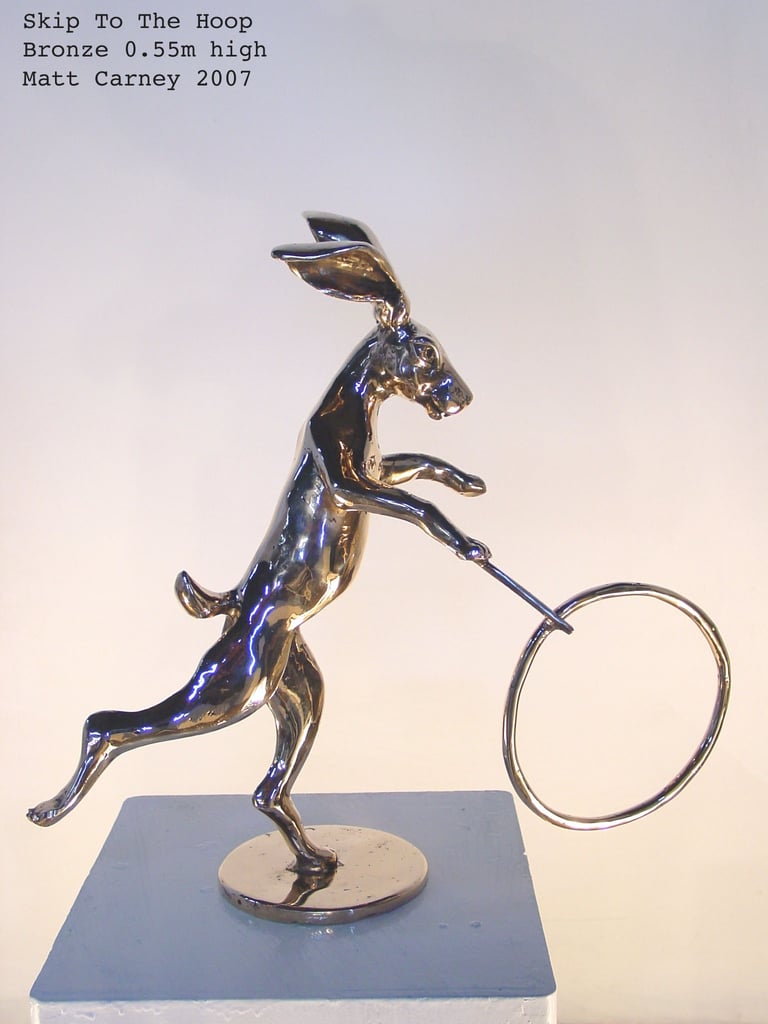 a bronze statue of a rabbit playing with a stick and hoop