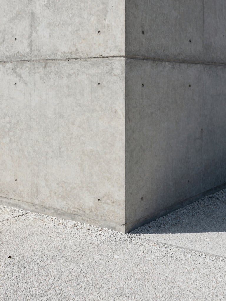 Close-up of a finished architectural concrete wall meeting a clean gravel pathway, sharp shadows, overcast light.