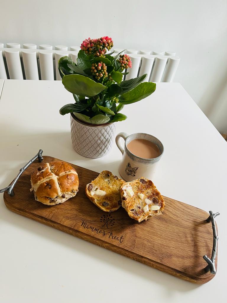 a wooden serving board with hot cross buns and a cup of tea