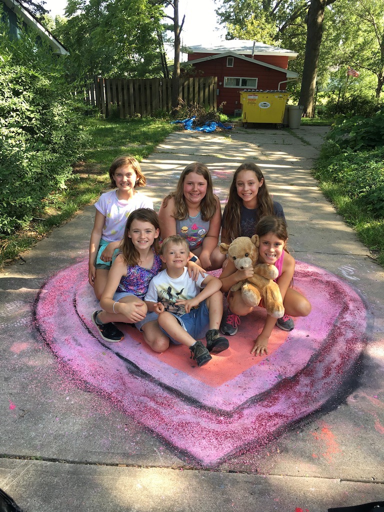 Group of smiling children posing on top of a large chalk heart they made.