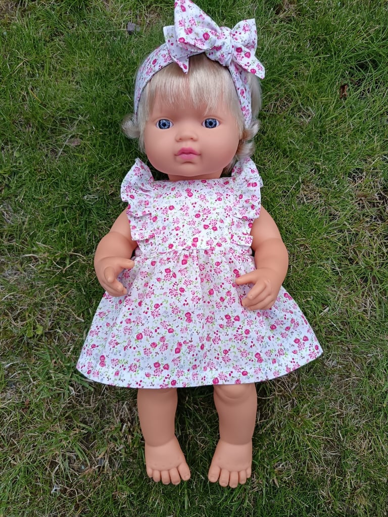 Miniland doll dressed in a pink floral dress with ruffles