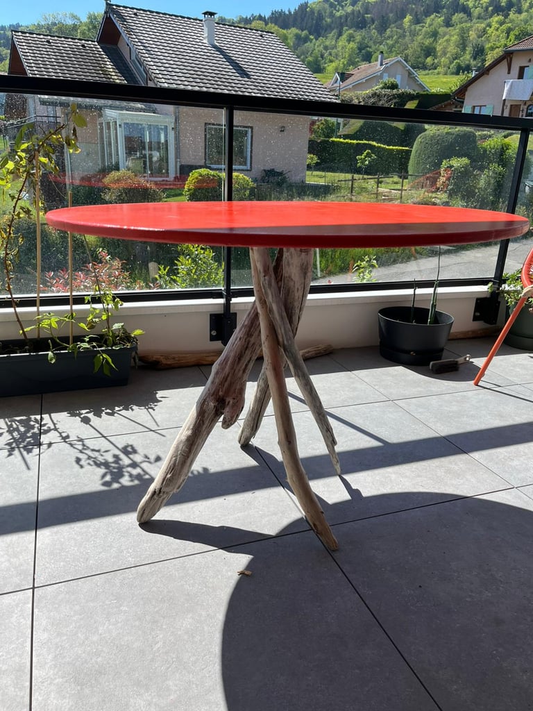 Handmade red round dining table with unique driftwood branch legs on a modern balcony patio.