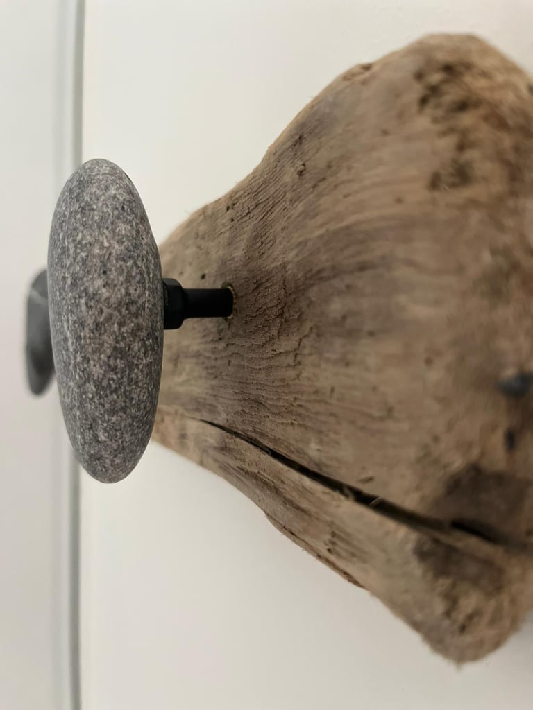 Rustic coat rack made of natural driftwood with smooth grey stone wall hooks.