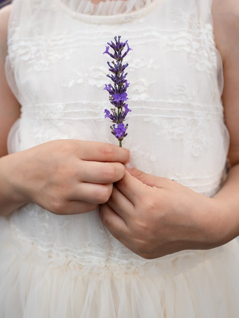 a little girl in a white dress and holding a stem of lavender