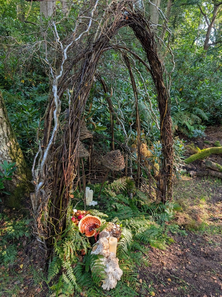 Rustic garden arch made of woven branches and vines with candles, ferns, and mushrooms.