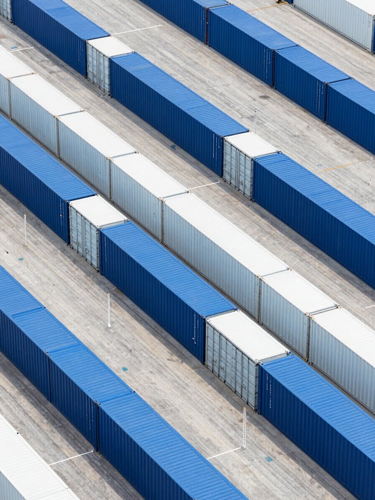 Overhead geometric shot of perfectly aligned blue and white shipping containers in a clean, modern dry port terminal, bright daylight