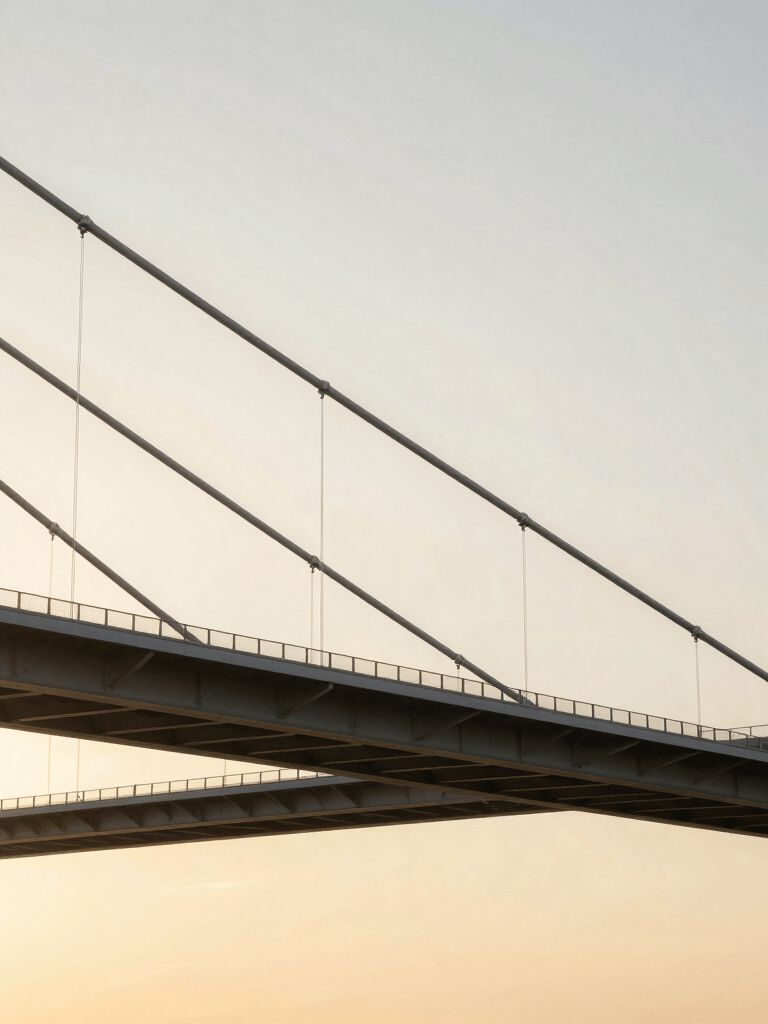 Wide shot of a contemporary architectural bridge suspended over a clean void, pure steel lines illuminated by a warm golden sunset.