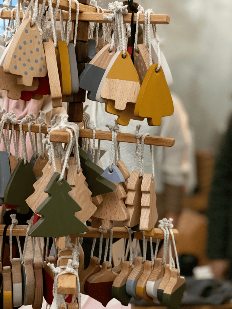 Handcrafted wooden Christmas tree ornaments in various colors hanging on a display stand at a craft market.