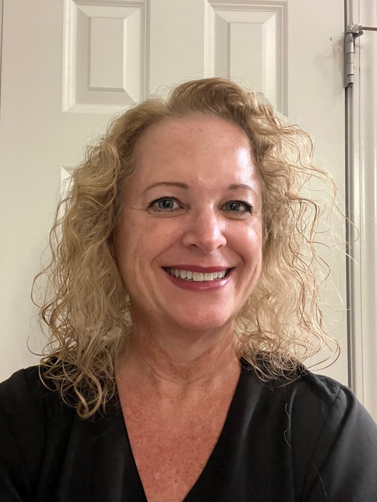 Smiling blonde woman with curly hair wearing a black shirt in front of a white door.