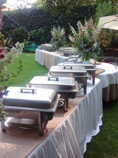 Servicio de taquiza en un jardín, diversos guisados en charolas calentándose listos para comer.