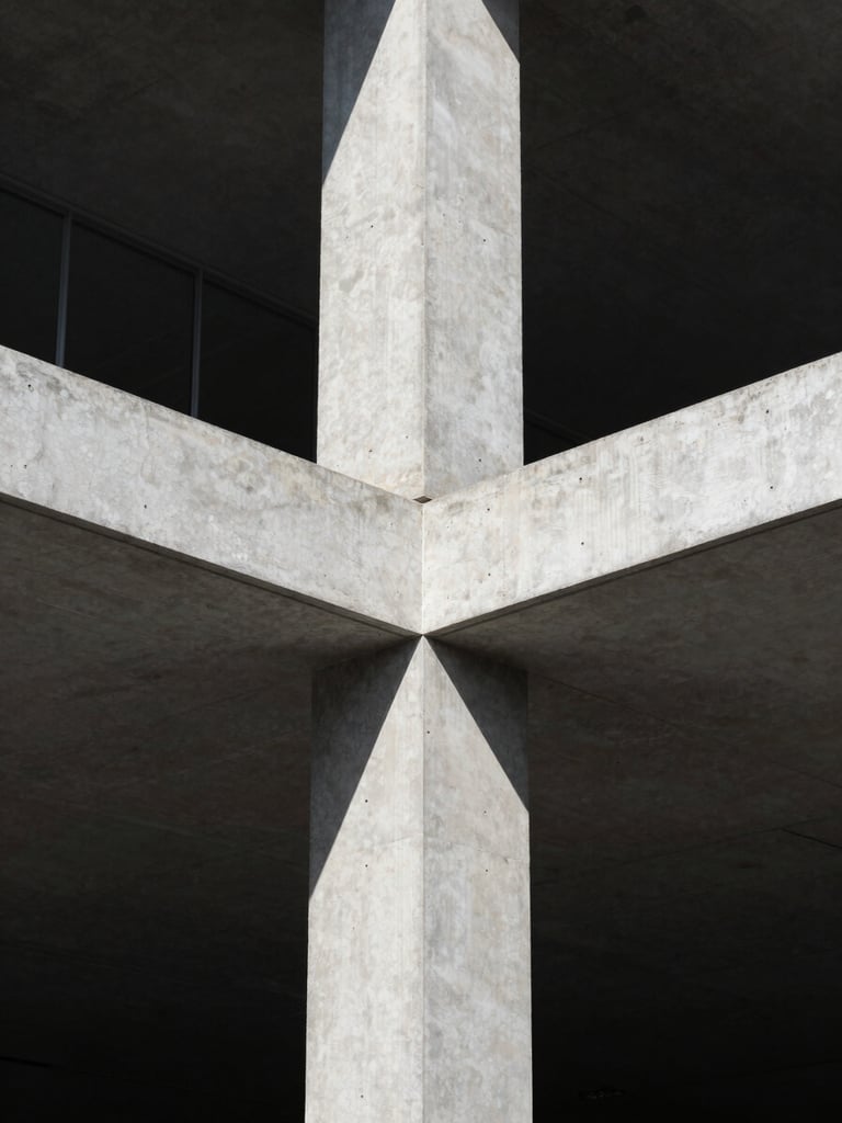 Portrait-oriented architectural photograph of a detailed structural join between concrete and steel, captured in harsh, directional sunlight, deep shadows highlighting texture.